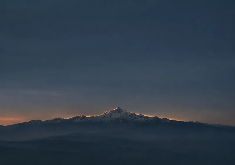 iPhone Duo alpine dusk wallpaper for the inner display, a wide snow-capped mountain ridge under a deep blue dusk sky with a thin amber horizon, 2670x1878 px